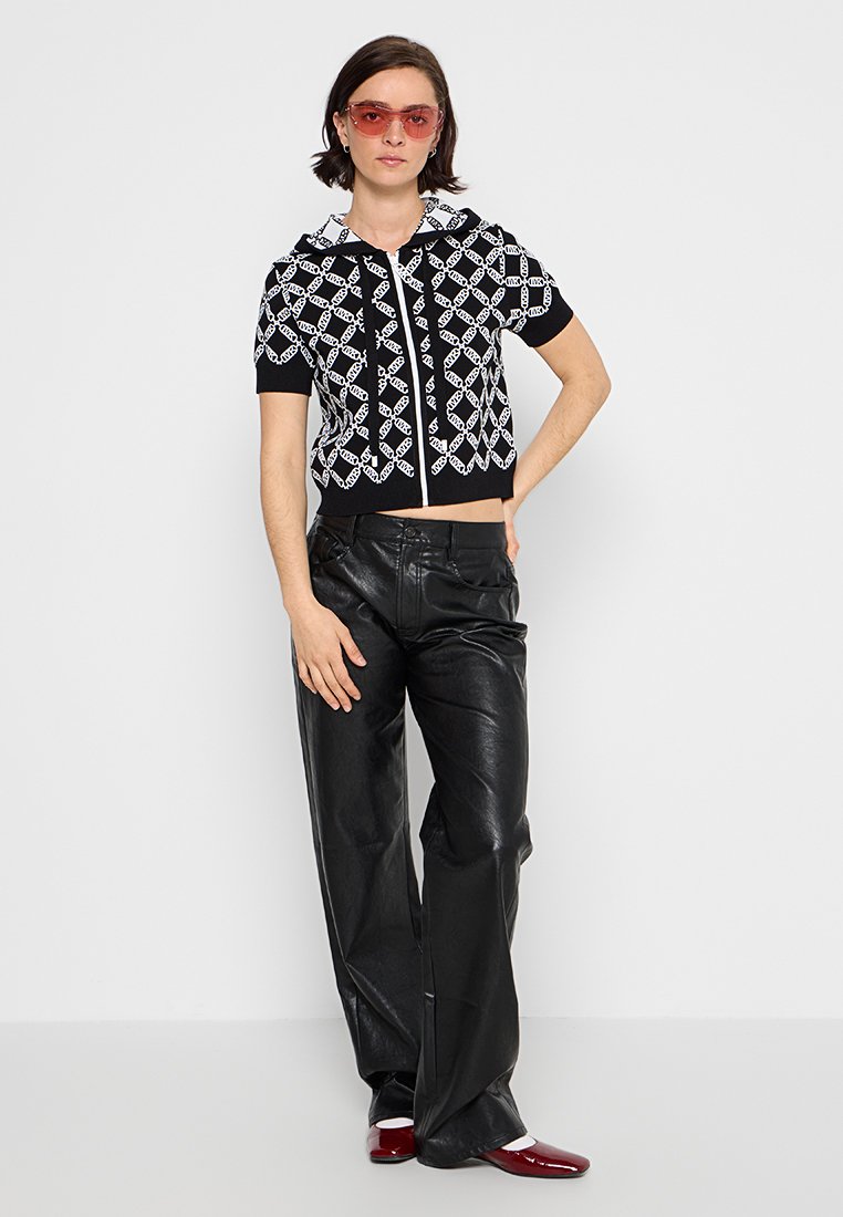 Zwart-wit gestreepte hoodie met korte mouwen en ritssluiting, gecombineerd met hoge zwarte leren broek en rode schoenen.