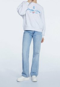 Grijze sweatshirt met de tekst "Brooklyn Bridge" in het blauw, gecombineerd met lichtblauwe flared jeans en witte sneakers. Casual outfit met een relaxte pasvorm.
