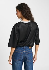 Black ribbed short-sleeve top with a round neckline and a silver trim, worn with blue high-waisted jeans featuring contrasting stitching.