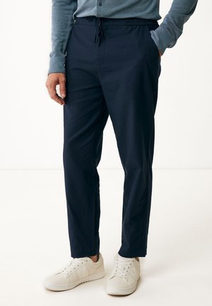 Marineblaue Hose mit elastischem Bund und Kordelzug, schmal geschnitten mit subtiler Textur. Kombiniert mit weißen Sneakers.