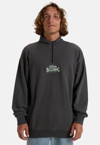Sweatshirt gris à col montant, avec une demi-fermeture éclair et un logo "BILLABONG" brodé en blanc et vert sur la poitrine. Tissu en mélange de coton.