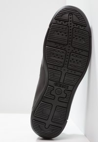 Semelle de chaussure en caoutchouc noir avec un motif texturé, comprenant des rainures de bande de roulement et des perforations. Logo Geox visible près de la base.