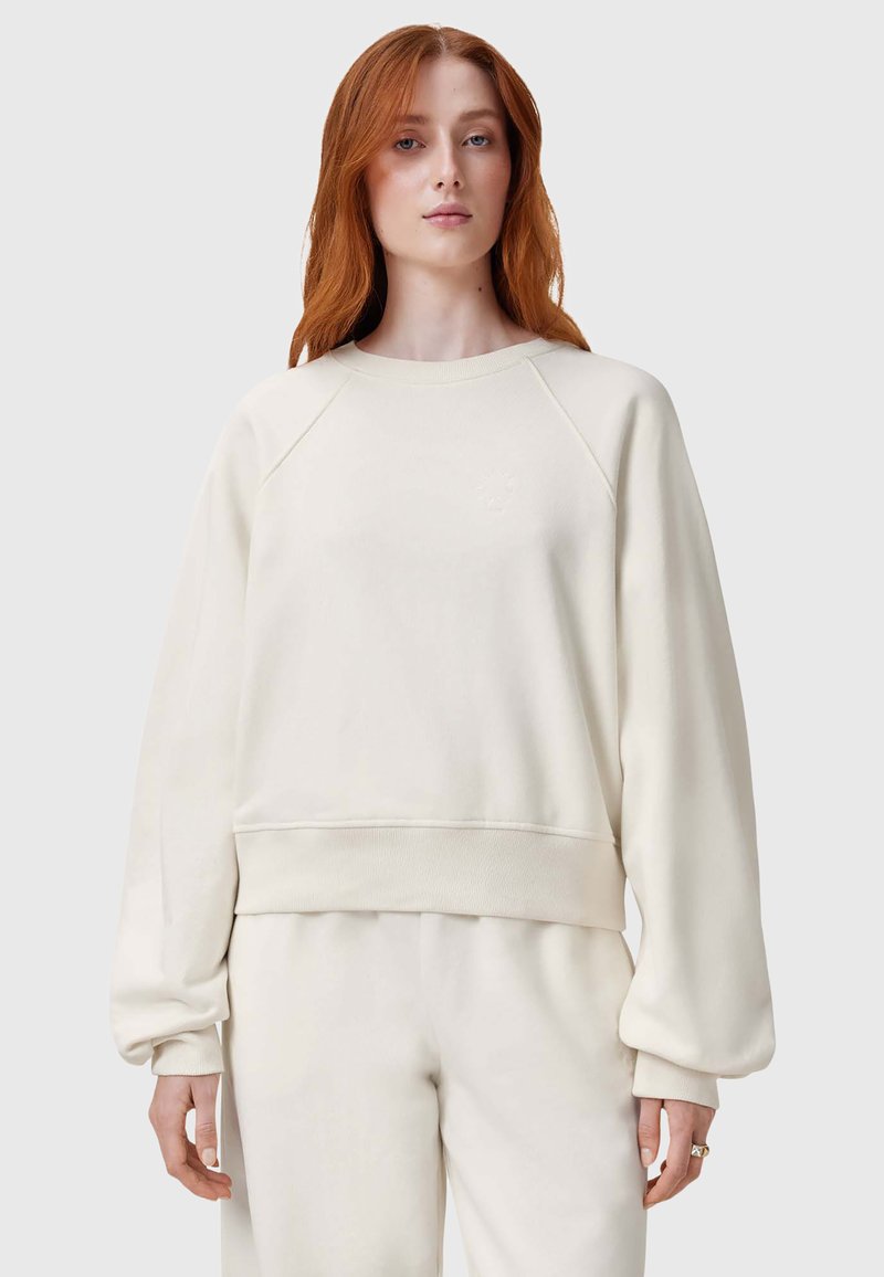 Sudadera color crema con mangas raglán largas, puños y dobladillo acanalados, que presenta un discreto logotipo bordado en el pecho. Textura suave.