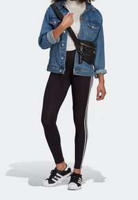 Black leggings with white side stripes, paired with a denim jacket and a black crossbody bag. Black and white sneakers complete the look.
