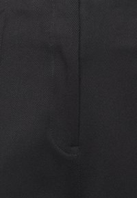 Czarne spodnie wykonane z teksturowanej tkaniny. Charakteryzują się gładkim przodem, skośną kieszenią oraz czystymi, dopasowanymi liniami.