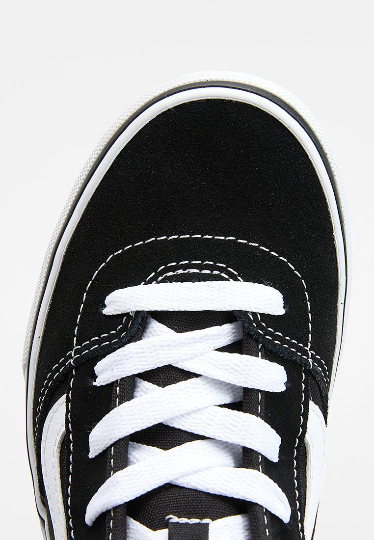 Zapatilla de ante negro con costuras y cordones blancos. Cuenta con una suela de goma blanca y un detalle lateral. Diseño plano con forma de puntera redondeada.