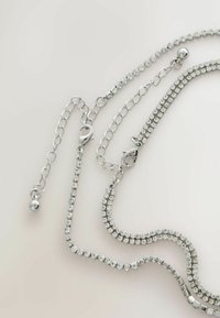 Stříbrný řetízek s více prameny, zdobený jasnými rhinestony různých tvarů a s karabinovým zapínáním pro bezpečné upevnění.