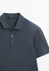 Mørkeblå polo i tekstureret stof med klassisk krave og tredobbelt knaplukning, korte ærmer og minimale syningsdetaljer.