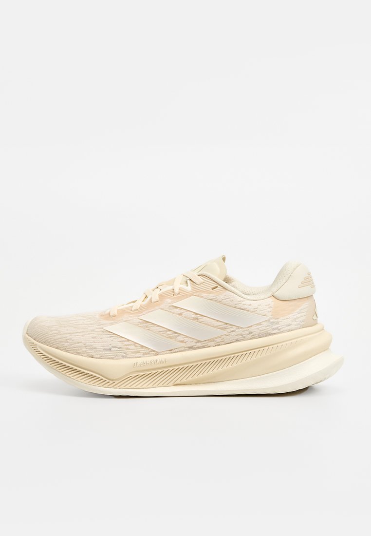 Zapatilla deportiva beige con parte superior texturizada, tres franjas blancas y una suela acolchada. Presenta un diseño aerodinámico y materiales sintéticos.