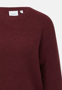 Burgundowy sweter dzianinowy o prążkowanej fakturze, okrągłym dekolcie i widoczną metką. Materiał wydaje się być miękki i nieco elastyczny.