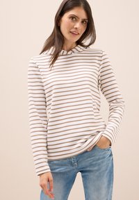Camiseta de manga larga con rayas horizontales en beige y blanco, con un alto cuello y fabricada en suave material de algodón, combinada con jeans de mezclilla.