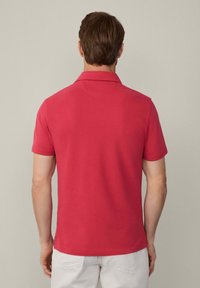 Červené polo tričko s uvoľneným strihom, krátkymi rukávmi a plochým golierom. Hladká textúra s jemnými stehovými detailami na leme.