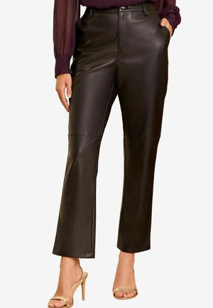 Pantalon en simili cuir noir avec une taille ajustée, une coupe droite, des coutures visibles et des poches latérales, associé à des sandales à talons dorées.