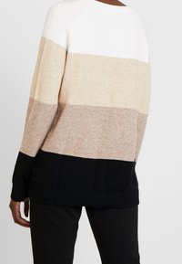 Maglione lavorato a maglia con strisce orizzontali bianche, beige, marrone chiaro e nere. Vestibilità rilassata con polsini e orlo a coste. Texture morbida.