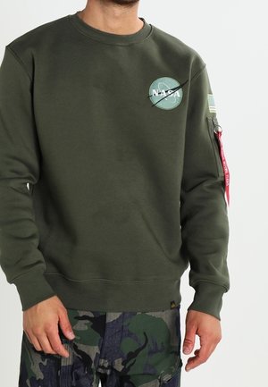 Olivgrüner Sweatshirt mit NASA-Logo und grafischen Details, ausgestattet mit gerippten Bündchen und Saum sowie einer Reißverschlusstasche am Ärmel mit rotem Tab.