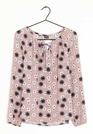 Blouse rose à manches longues avec motif floral noir, blanc et beige, col rond avec lien, présentée sur un cintre noir sur fond blanc.
