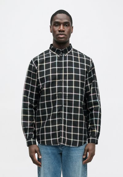 Μαύρο πουκάμισο με καρό σχέδιο και πολύχρωμες γραμμές, κουμπωτό, με γιακά και μακριά μανίκια, συνδυασμένο με ανοιχτόχρωμο τζιν παντελόνι.