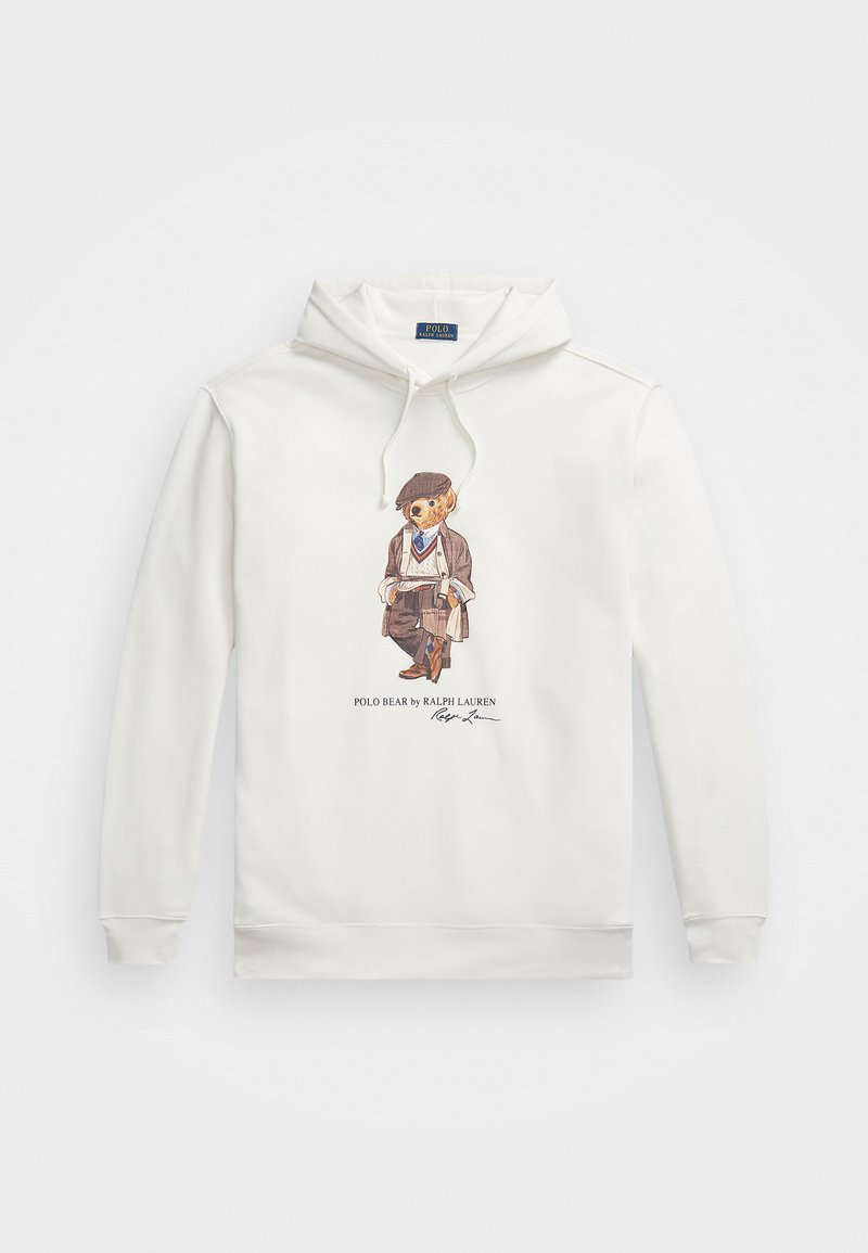 Valge kapuutsiga särk, mille esiküljel on trükitud karu pilt, kes kannab lamedat mütsi, bleiserit, kampsunit ja salli, hoides rulli keeratud paberit, koos tekstiga Polo Bear by Ralph Lauren.