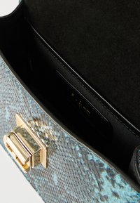 Δερμάτινη τσάντα χειρός με μπλε και μαύρο μοτίβο δέρματος φιδιού, χρυσά μεταλλικά στοιχεία και εσωτερικό επενδυμένο με απαλό σουέντ, με ετικέτα του brand.