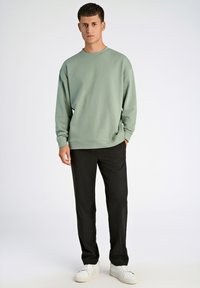 Jasnozielona bluza o luźnym kroju, z ribbowymi mankietami i okrągłym dekoltem, w połączeniu z czarnymi spodniami i białymi trampkami.