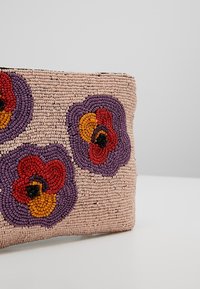 Pochette beige ornée de perles avec des motifs floraux violets, rouges, orange et noirs sur un fond uni gris clair.