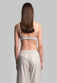 Vaaleanharmaa bralette säädettävillä olkaimilla ja ryppyperällä, yhdistettynä vaaleanraidallisiin housuihin, joissa on joustava vyötärö ja takataskut.