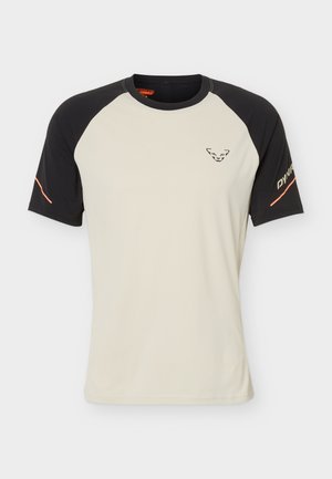 Sportska majica kratkih rukava s bež tijelom, crnim raglan rukavima, malim crnim logotipom na prsima i tekstom "DYNA" na desnom rukavu u narančastoj boji.