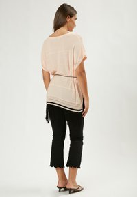 Helles Pfirsich oversized Oberteil mit einer Häkel-Details am Rücken, kombiniert mit schwarzen Cropped-Hosen mit Spitzenakzenten am Saum.
