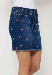 Jeans krilo s prilagojeno zasnovo, modre barve, raztrgan rob in roza vezeni cvetlični vzorci po celotnem krilu.
