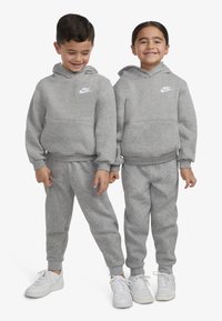 Grå hettegensere og bukser laget av mykt stoff, med Nike-logo, kombinert med hvite joggesko.