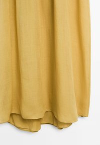 Gelbes Leinenkleid mit weicher Textur. Der Saum ist leicht geschwungen, und das Material wirkt leicht und fließend.