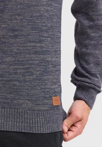 Maglione lavorato a maglia blu navy con motivo testurizzato, polsini e orlo a coste, caratterizzato da un'etichetta in pelle beige sul lato inferiore.