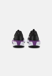 Chaussures de sport noires avec des accents violets, dessus en mesh, tissu texturé, et une semelle blanche robuste ; languette au talon pour un enfilage facile.