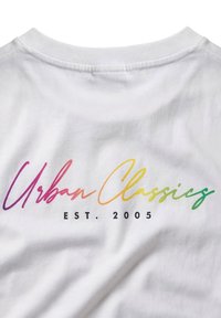 Λευκό T-shirt με την επιγραφή "Urban Classics" σε κείμενο με διαβάθμιση ουράνιου τόξου και την ένδειξη "EST. 2005" τυπωμένη με μαύρο κάτω από το κείμενο στο πάνω μέρος της πλάτης.