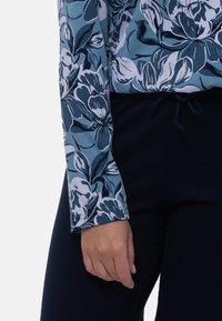 Blomstret langærmet top i blå og grå nuancer, med rund halsudskæring og tætsiddende ærmer, parret med mørke elastiske bukser med taljebånd.