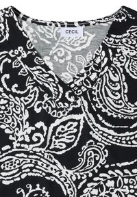 Tissu à motif cachemire noir et blanc avec un col en V et une étiquette de la marque CECIL cousue à l’encolure.
