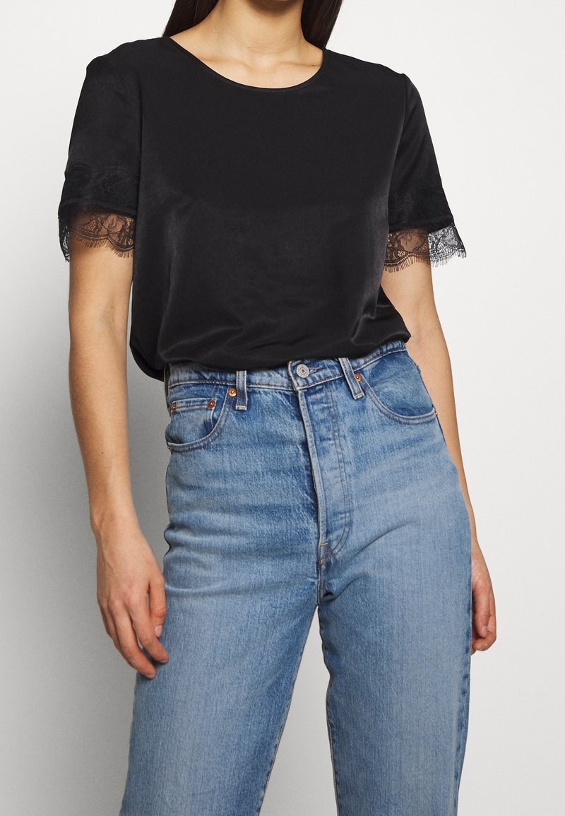 Sort kortærmet skjorte med blondekant, rund halsudskæring, parret med lys blå high-waisted jeans, der har en klassisk pasform og denimtekstur.