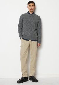 Grauer Strickpullover, beiger Cargo-Hose, schwarze Schuhe. Das Outfit besteht aus einem strukturierten Pullover und Utility-Style-Hosen mit Seitentaschen.