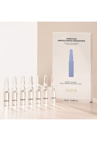 Ampoules en verre transparent contenant un sérum liquide, disposées en rangée, avec une boîte blanche comportant des graphiques bleus et un texte noir, étiquetée "HYDRA PLUS."