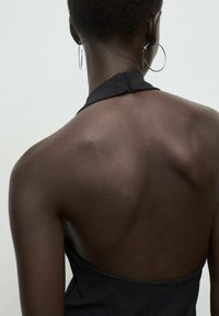 Vestido negro de cuello halter con la espalda descubierta, tejido suave y textura lisa, que resalta los omóplatos prominentes y grandes pendientes de aro.