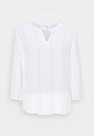 Blouse blanche à manches longues avec fines rayures verticales, col rond, ouverture en forme de goutte et nœud noué à l'avant.