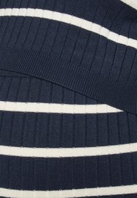 Tissu côtelé bleu marine avec des rayures blanches horizontales, montrant une section pliée mettant en valeur la texture et le motif.