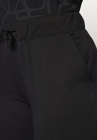 Sorte joggesko laget av myk stoff, med elastisk midje med snor og sidelommer. Glatt tekstur, tettsittende design.