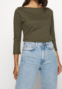 Maglia a maniche lunghe verde oliva con scollatura a barca, abbinata a jeans chiari a vita alta con un classico design a cinque tasche.