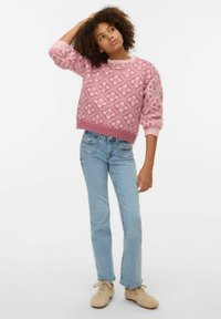 Ružičasti džemper s uzorkom, širokog kroja i rebrastim manšetama, uparen s ravnim trapericama svijetloplave boje i bež tenisicama. Jednostavna pozadina.