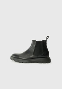 Bottines Chelsea noires en cuir lisse, dotées de panneaux latéraux élastiques, d'une semelle rembourrée et d'une languette au talon pour un enfilage facile.
