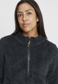 Gray, fleece zip-up jacket with a high collar and soft texture. Features a zipper closure and a small leather accent near the zipper.