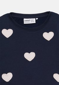 Παιδικό πουκάμισο σε ναυτικό μπλε με στρογγυλή λαιμόκοψη, διακοσμημένο με πέντε λευκές καρδιές με ραφές, ομοιόμορφα τοποθετημένες.