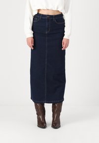 Σκούρο μπλε τζιν μίνι φούστα με μπροστινή ραφή, ψηλή μέση και ίσια γραμμή. Συνδυάζεται με καφέ μπότες μέχρι το γόνατο για αντίθεση.