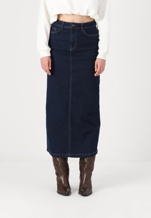 Jupe midi en denim bleu foncé avec une couture avant, taille haute et coupe droite. Associée à des bottes marron jusqu'aux genoux pour un contraste.